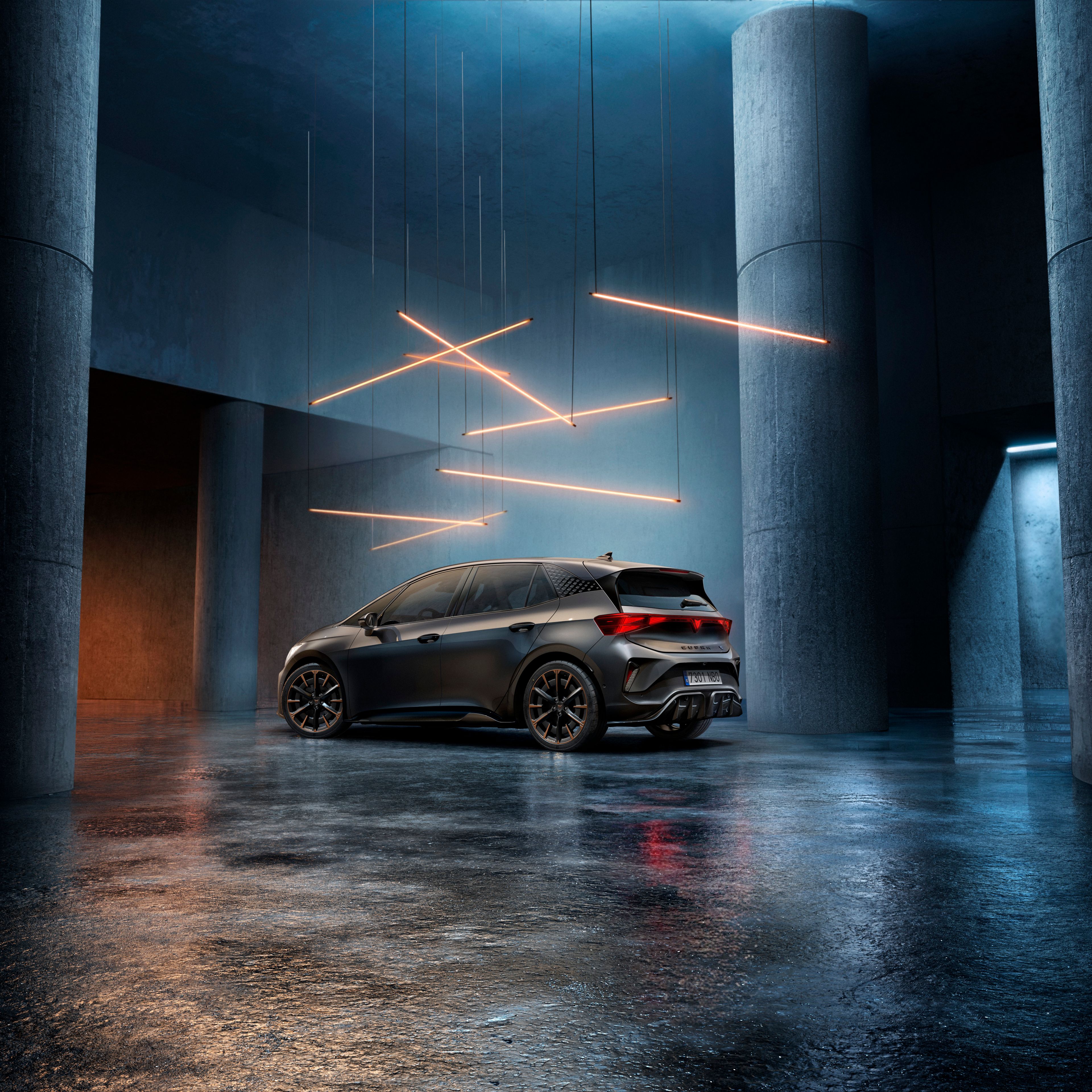 CUPRA Born stojí v štýlovo osvetlenom priemyselnom priestore s betónovými stenami a stĺpmi. Zo stropu visí niekoľko lineárnych svetelných zdrojov, ktoré vytvárajú elegantnú atmosféru. Vozidlo je vidieť zo zadnej strany a odráža svetlo na lesklej podlahe.