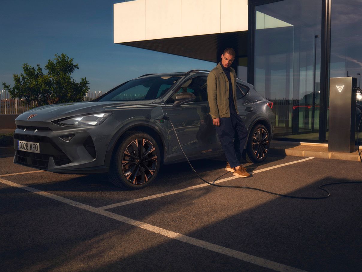 CUPRA Formentor e-Hybrid pri nabíjaní pred modernou budovou. Muž sa opiera o vozidlo.