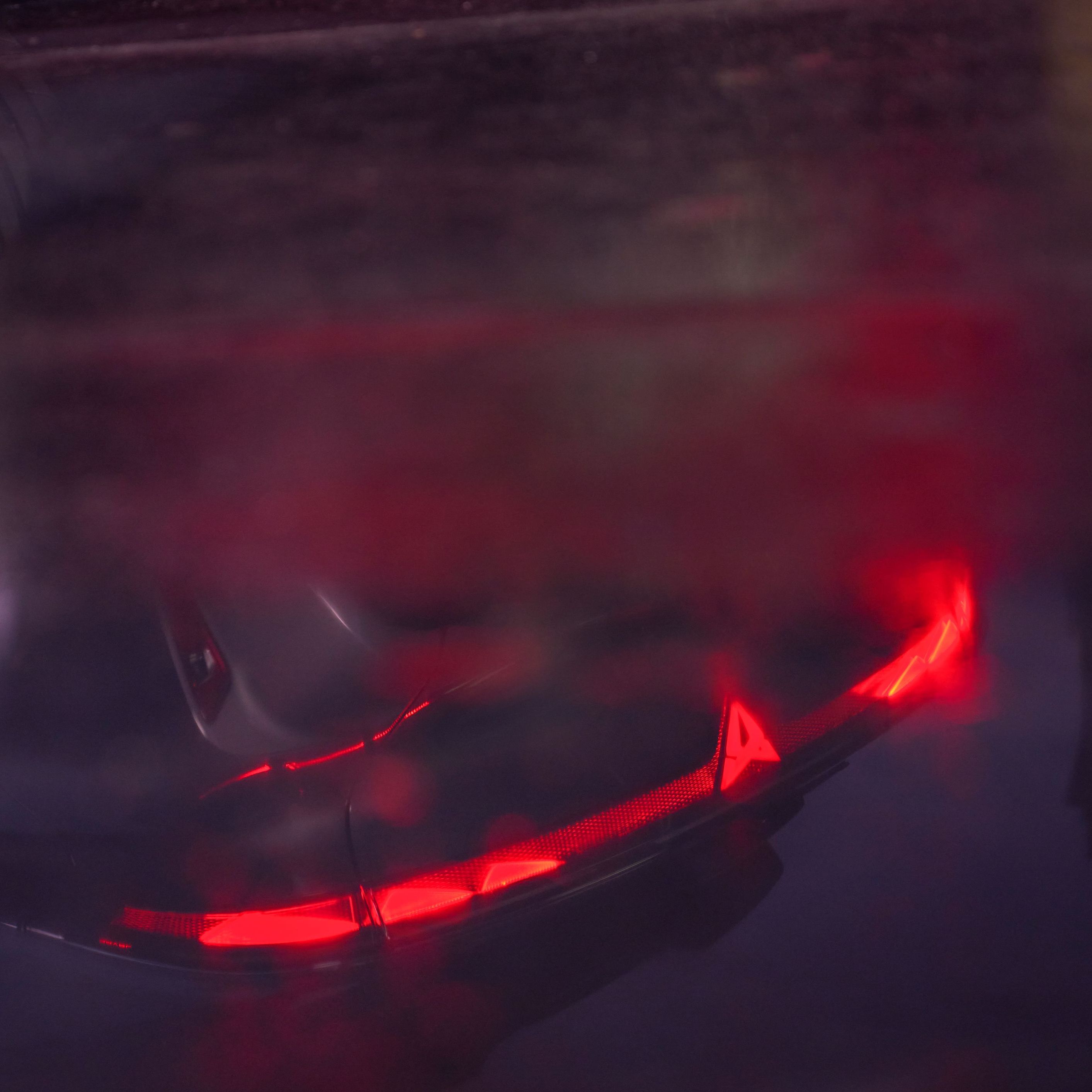 Pohľad na tmavú, mokrú podlahu, v ktorej sa odráža nový model Raval. Detail na zasvietené zadné svetlá.