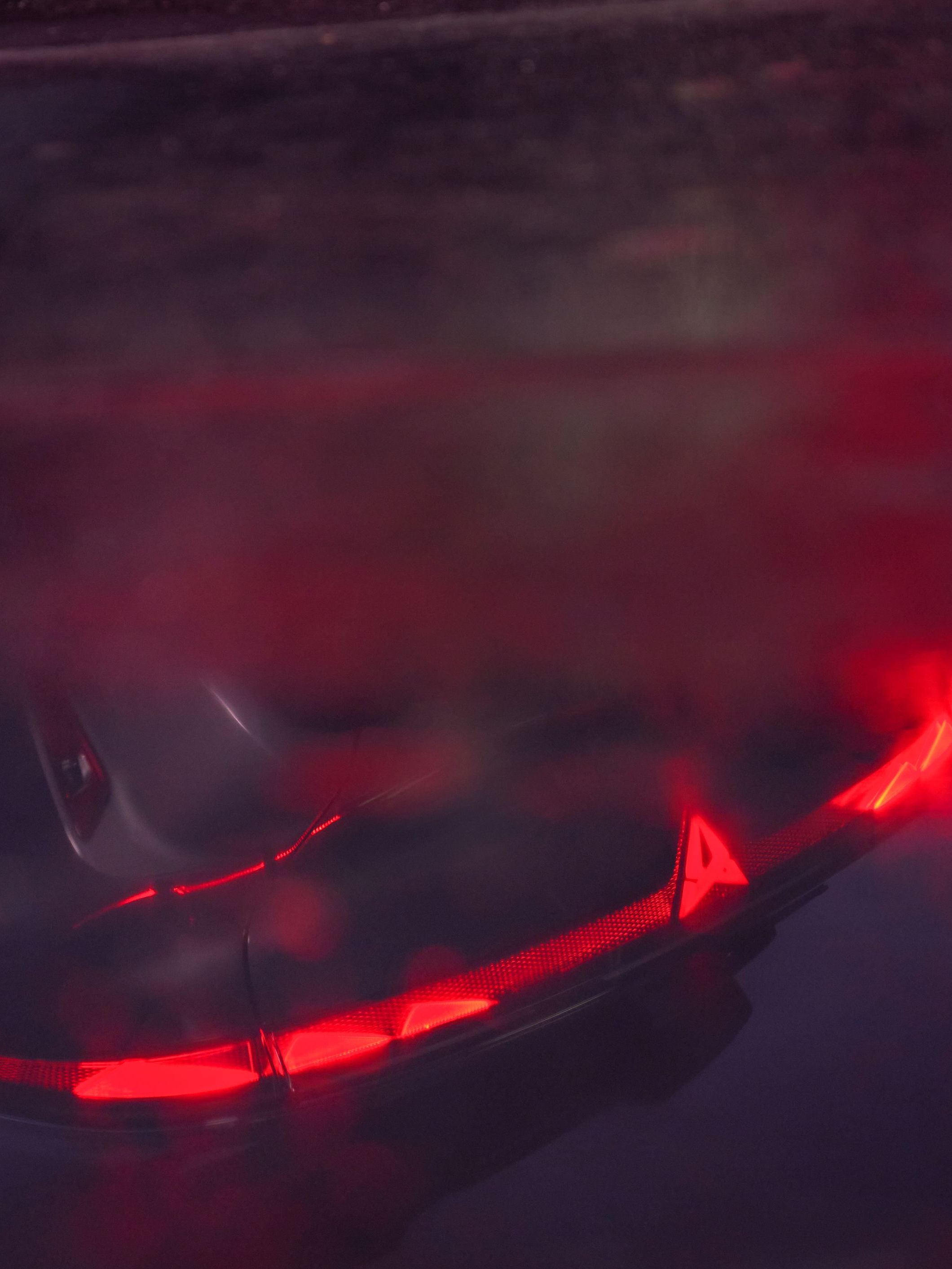 Pohľad na tmavú, mokrú podlahu, v ktorej sa odráža nový model Raval. Detail na zasvietené zadné svetlá.