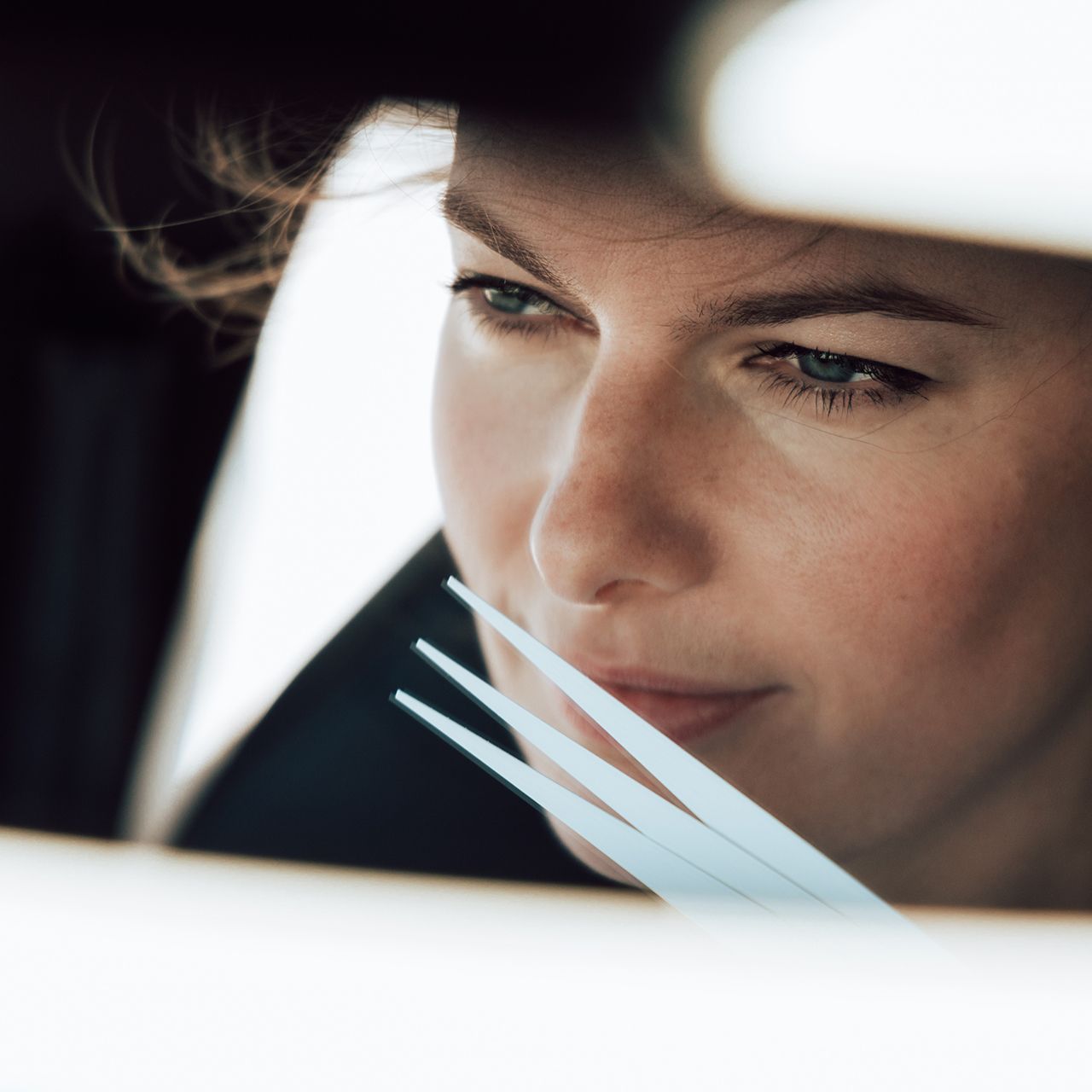 Žena sedí v aute. Má hnedé vlasy. Jej obraz zreteľne vidieť v spätnom zrkadle.