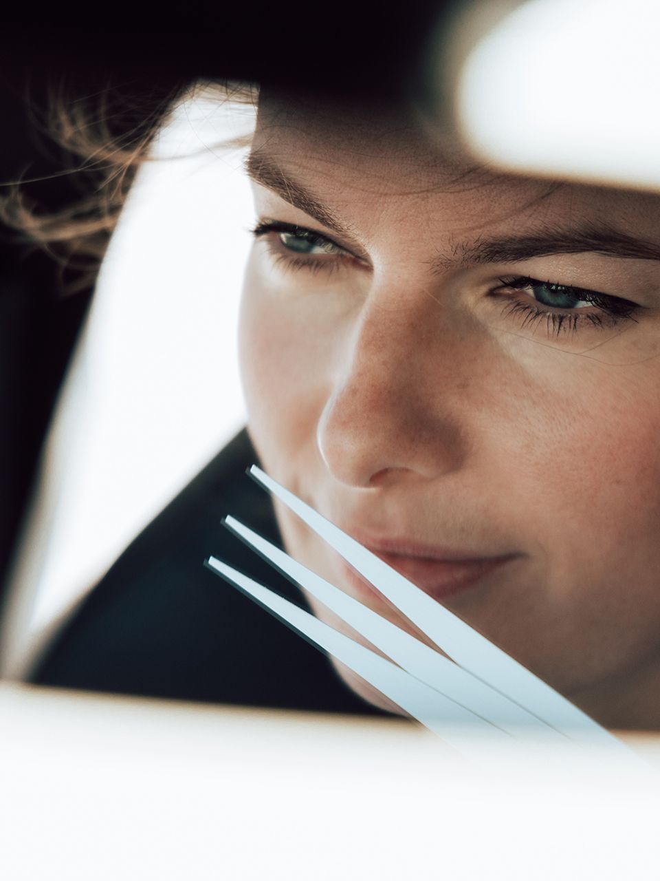 Žena sedí v aute. Má hnedé vlasy. Jej obraz zreteľne vidieť v spätnom zrkadle.