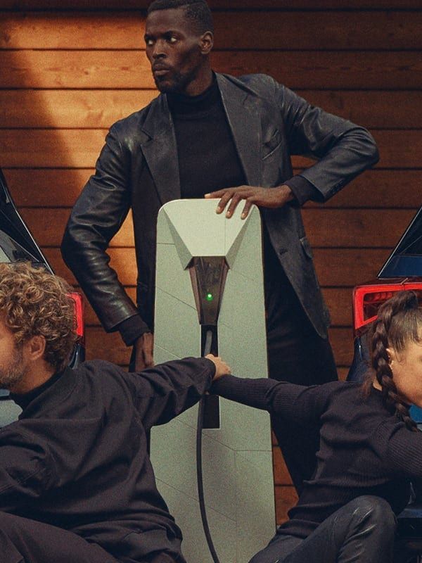 Skupina štyroch osôb v čiernom drží navzájom svoje ruky pred dvomi modrými autami Cupra. Postava v strede stojí, zvyšok sedí na zemi. 