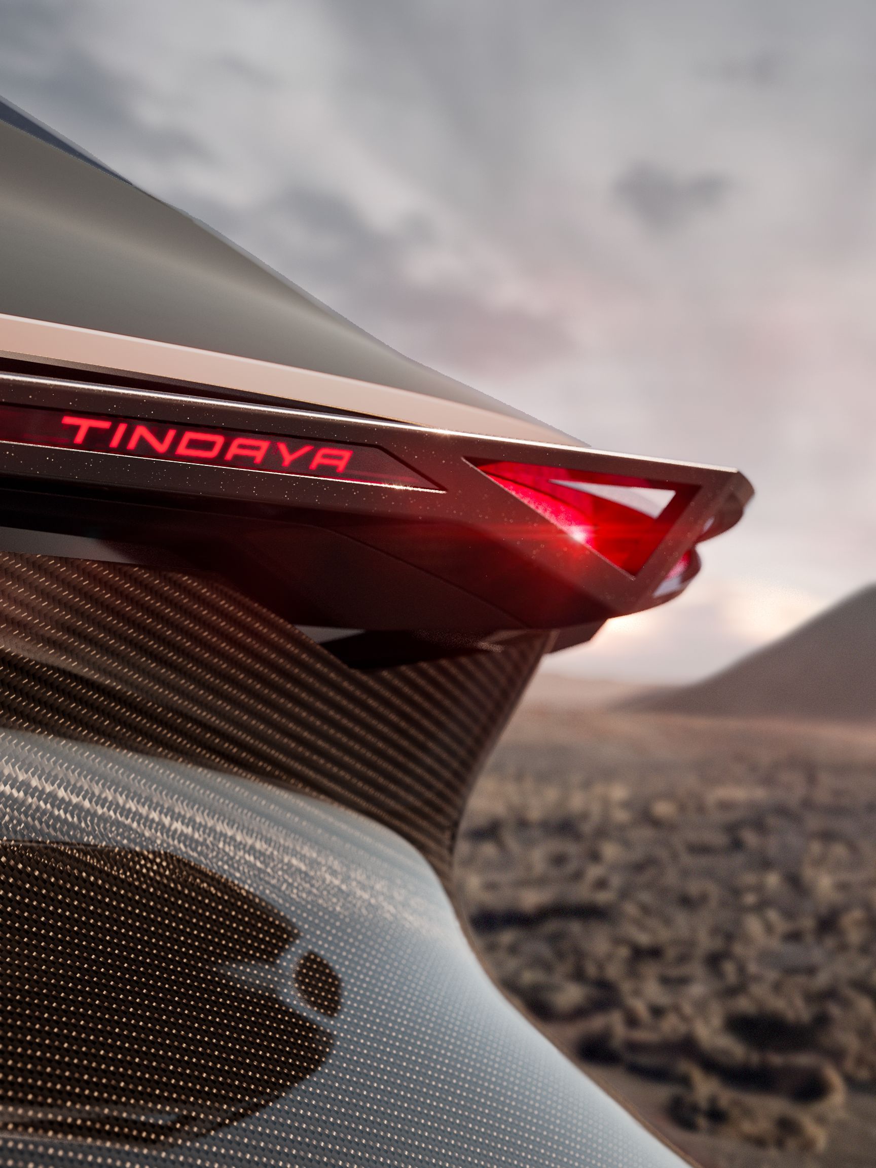 Detailný záber na zadné svetlo futuristického automobilu s názvom 'TINDAYA'. V pozadí je krajinná scenéria, pravdepodobne púšť alebo kamenistá planina. Svetlo svieti červenou farbou.