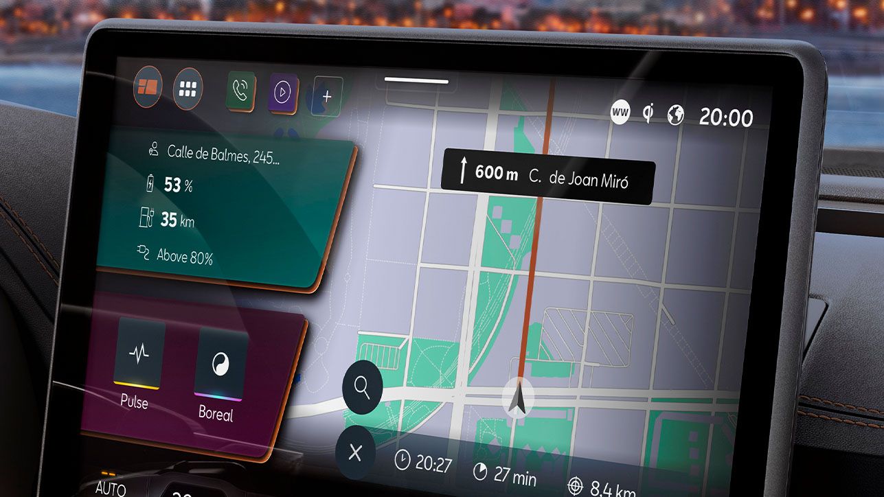 Detail na dotykový displej systému infotainment, ktorý zobrazuje mapu a navigačné pokyny. Sú zobrazené údaje o batérii a rôzne možnosti navigácie. V pozadí sa nachádza panoráma mesta, ktorú vidieť cez okno auta.