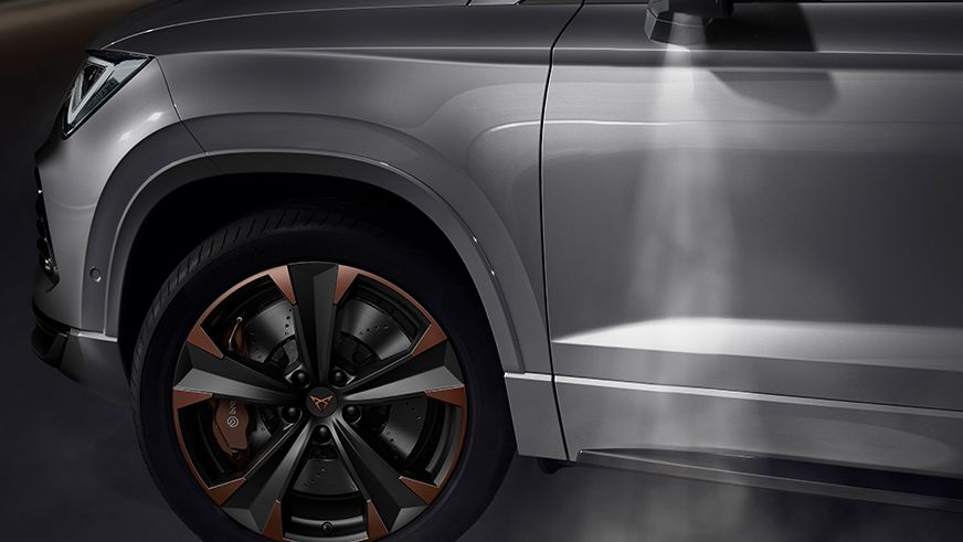 Detailný pohľad na predné koleso moderného auta s čiernymi diskami s bronzovými prvkami. Zrkadlo premieta logo značky na zem. 