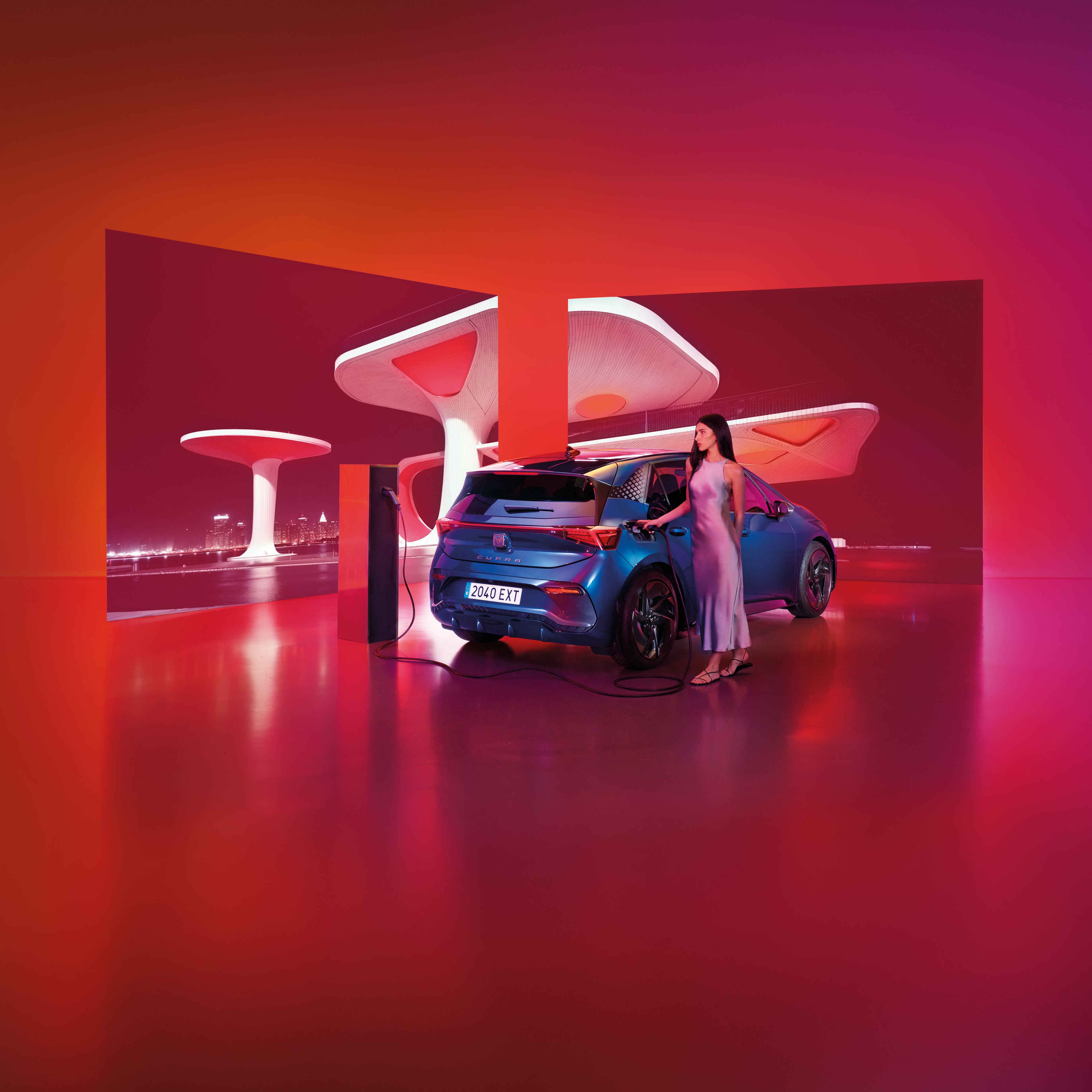 Moderne futuristické prostredie s červeno-ružovým osvietením, žena nabíja modré športové auto na elektrickej nabíjačke. Automobil vyniká výrazným aerodynamickým dizajnom. Pozadie tvorí neobvyklá architektúra so zaoblenými bielymi štruktúrami.