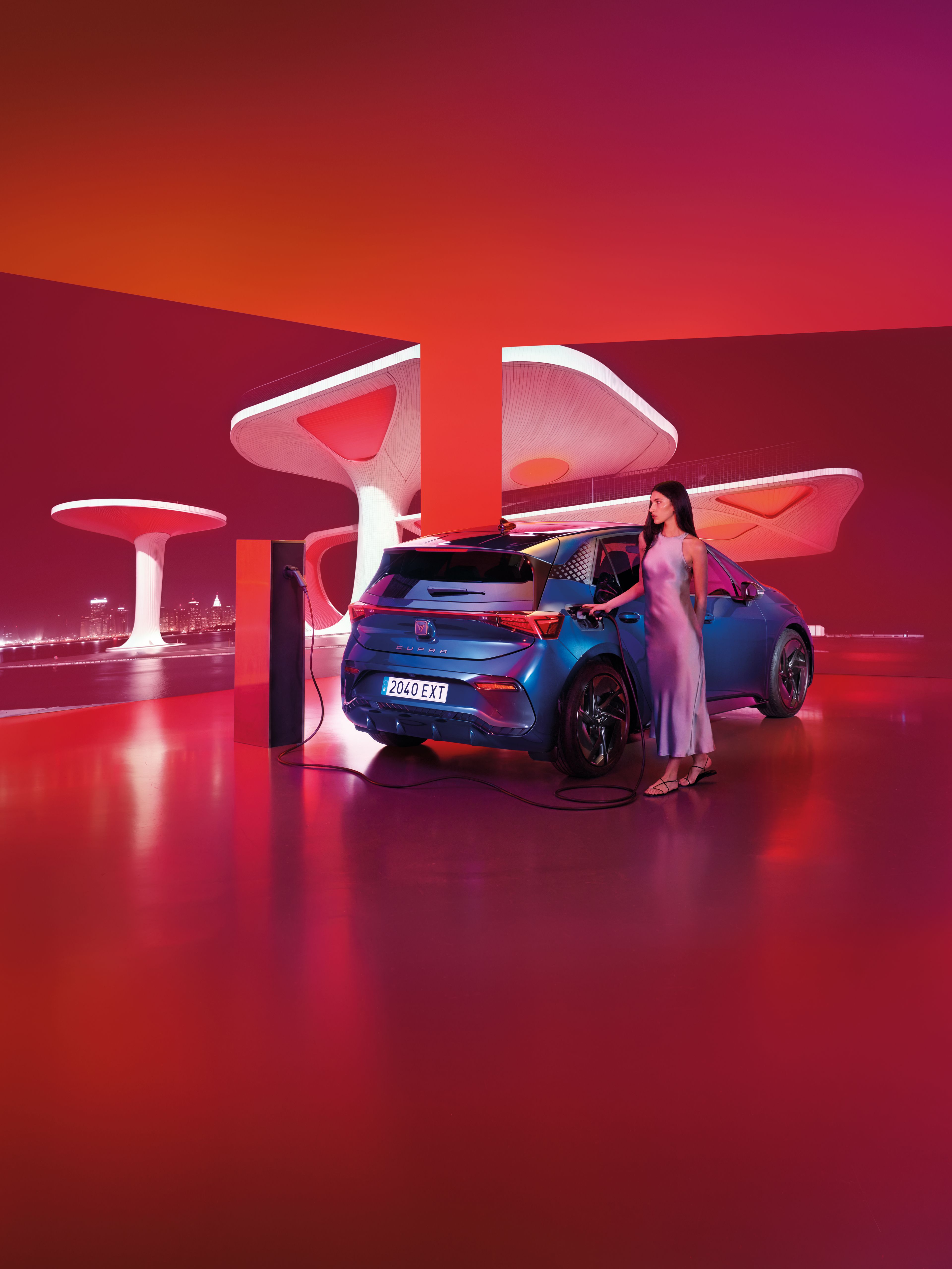 Moderne futuristické prostredie s červeno-ružovým osvietením, žena nabíja modré športové auto na elektrickej nabíjačke. Automobil vyniká výrazným aerodynamickým dizajnom. Pozadie tvorí neobvyklá architektúra so zaoblenými bielymi štruktúrami.