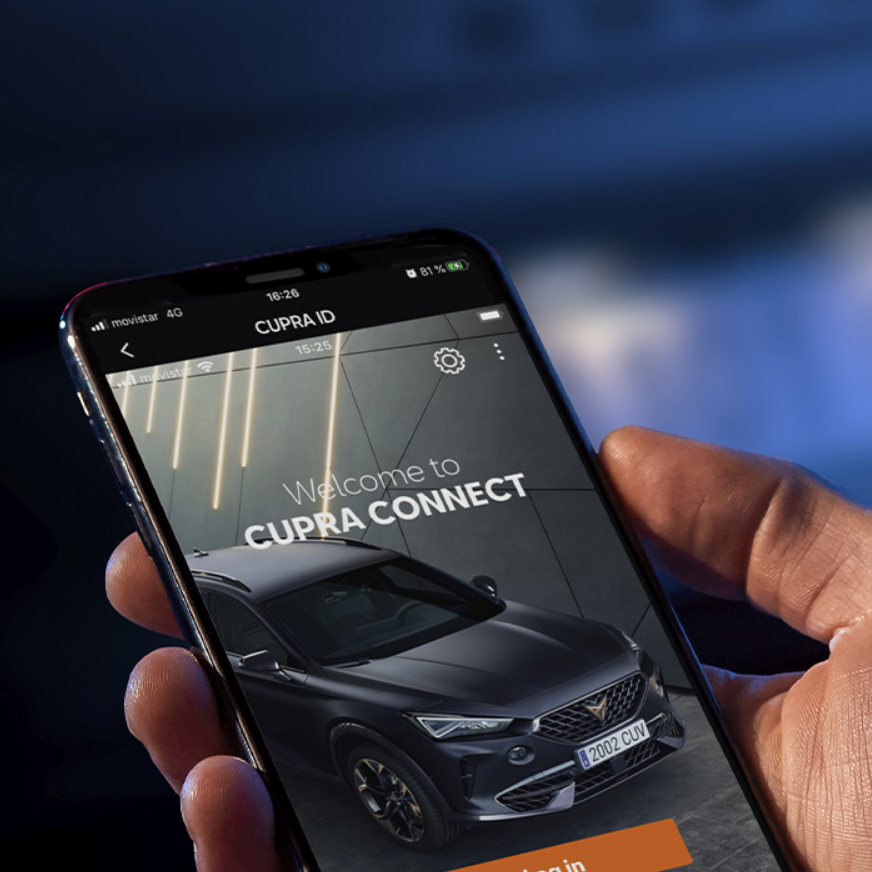 Ruka drží mobilný telefón, na ktorého displeji sa zobrazuje aplikácia CUPRA CONNECT. Na displeji je obrázok auta CUPRA a tlačidlo s textom "Log in". V pozadí je rozmazané modré svetlo.