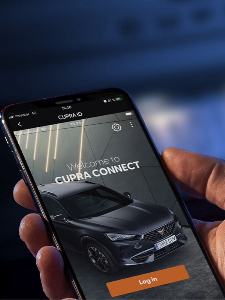 Ruka drží mobilný telefón, na ktorého displeji sa zobrazuje aplikácia CUPRA CONNECT. Na displeji je obrázok auta CUPRA a tlačidlo s textom "Log in". V pozadí je rozmazané modré svetlo.