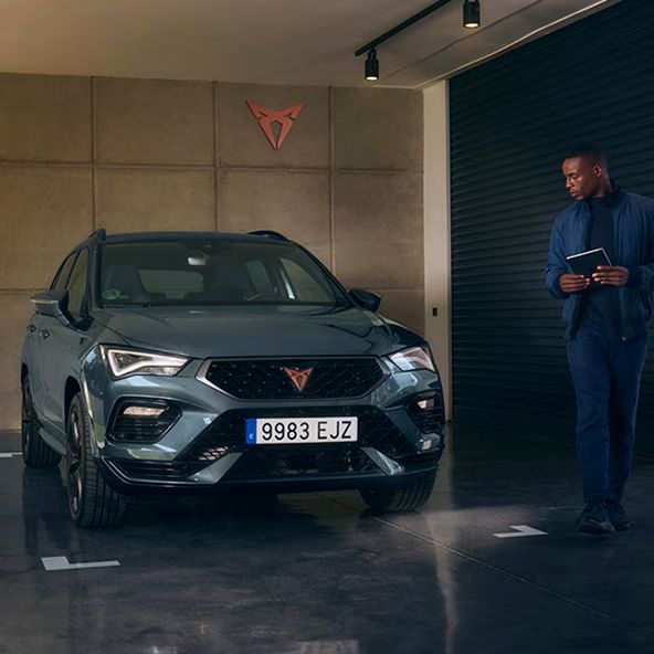 CUPRA Born zaparkovaný v garáži s hnedou stenou za vozidlom a logom CUPRA. Muž stojí vedľa vozidla a pozerá sa na neho