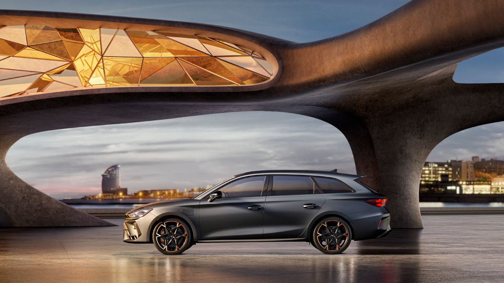 CUPRA Leon Kombi z bočného pohľadu zaparkované pri modernej, futuristickej budove. V pozadí je výhľad na panorámu nočného mesta.