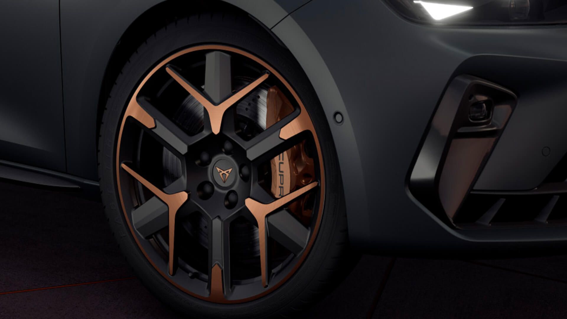 Detail na predné koleso športového auta. Koleso má čierny disk s bronzovými prvkami. V pozadí je vidieť časť predného nárazníka auta so svetlom do hmly.
