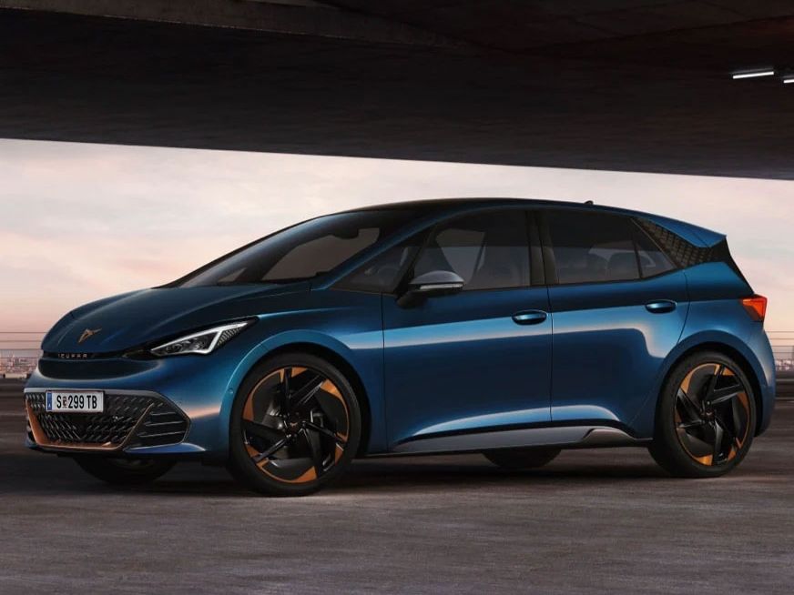 Tmavomodrý CUPRA Born, zaparkovaný pod betónovým mostom, s čiernymi diskami s bronzovými prvkami. Na auto dopadajú jemné lúče svetla, ktoré zvýrazňujú jeho moderný dizajn. 