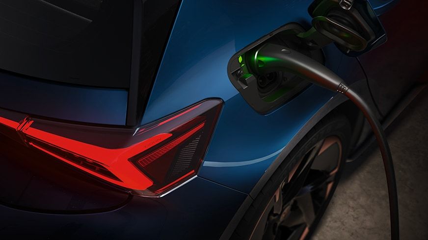 Elektrické SUV vozidlo modrej farby je nabíjané cez nabíjací kábel. Zadná časť vozidla je zvýraznená červeným svetlom. Nabíjací port svieti zeleným svetlom, čo značí nabíjanie.