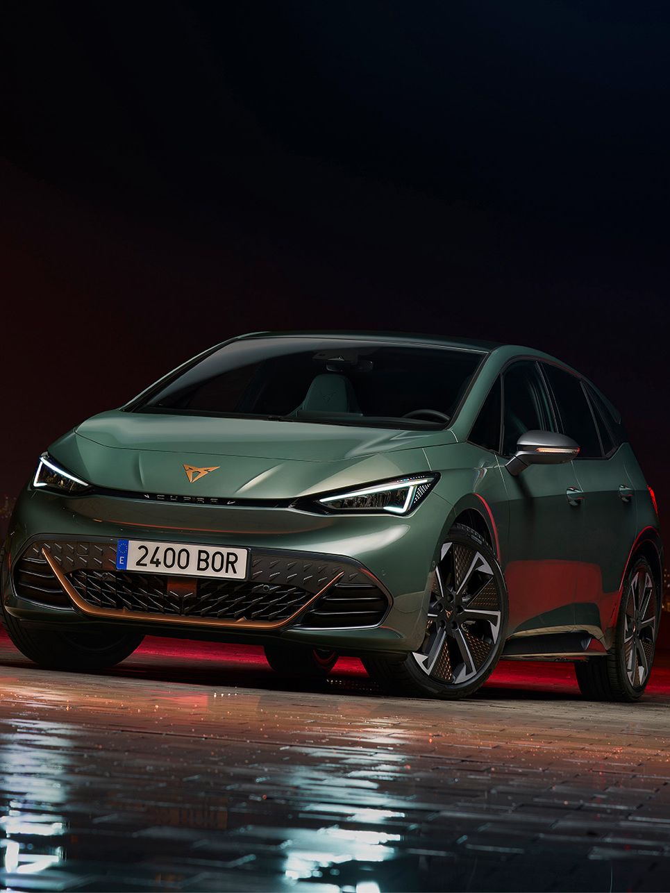 Tmavozelené športové vozidlo parkuje na mokrom parkovisku v noci. V pozadí sú osvetlené mestské budovy. Tento automobil má moderný dizajn a štýlové svetlá.