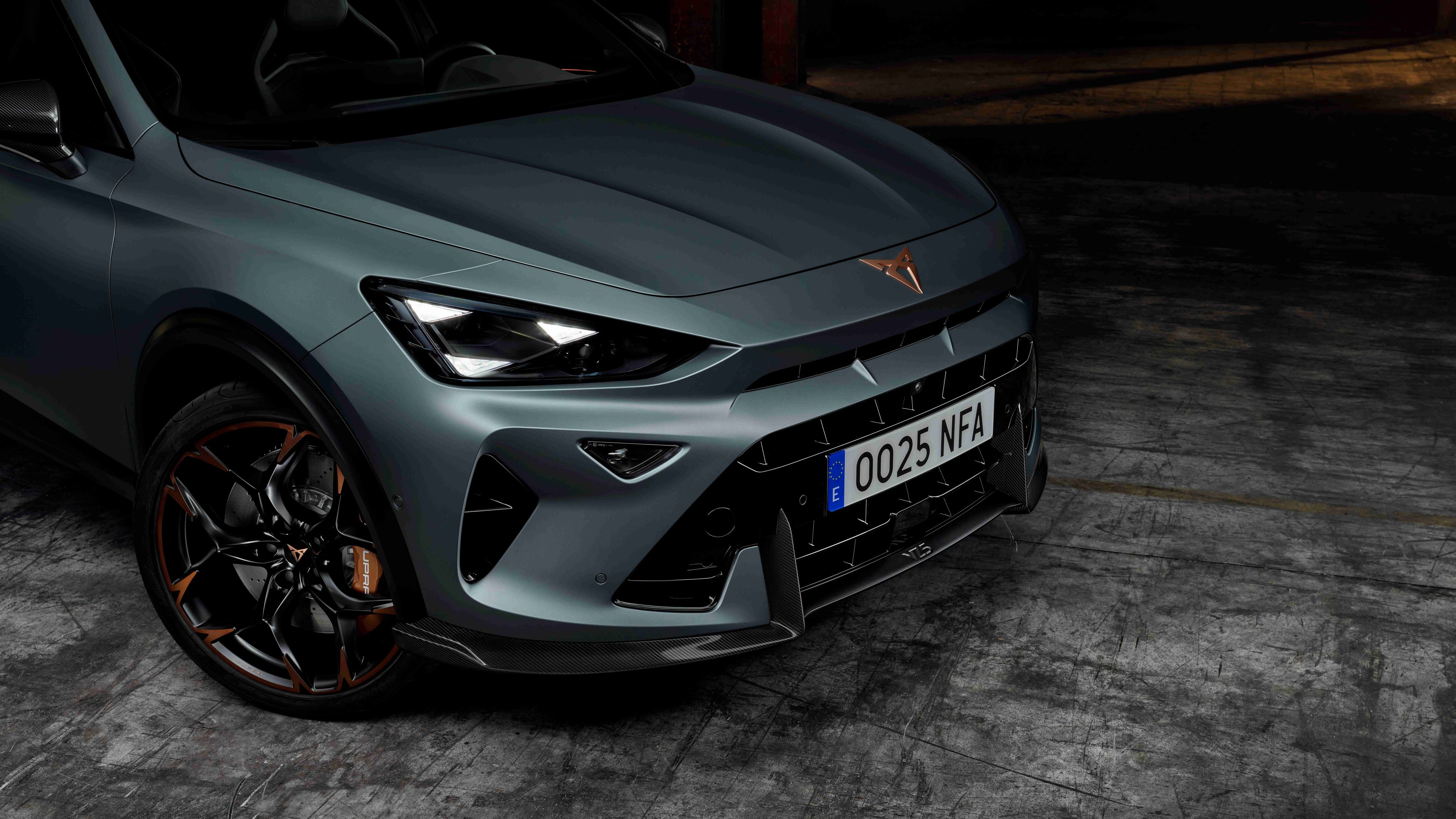Zelený športový automobil značky Cupra je zaparkovaný na tmavom povrchu. Predný nárazník obsahuje ostré línie a výrazný dizajn, zatiaľ čo kolesá majú lesklé čierne ráfiky.