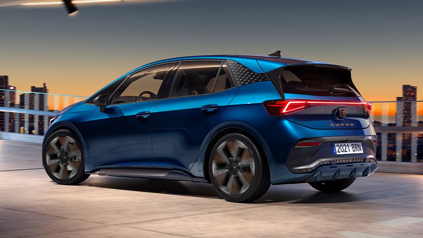 Modrý CUPRA Born je zaparkovaný na streche parkovacieho domu. V pozadí je večerná panoráma mesta. Vozidlo má moderný dizajn so svetlami LED.