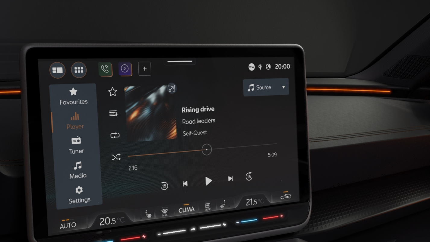 Dotykový displej systému infotainment v interiéri auta zobrazuje možnosti prehrávania hudby, nastavenia klimatizácie a ďalšie ovládacie prvky. Na displeji je zobrazená skladba s názvom "Rising Drive". Ambientné osvetlenie lemuje palubnú dosku..