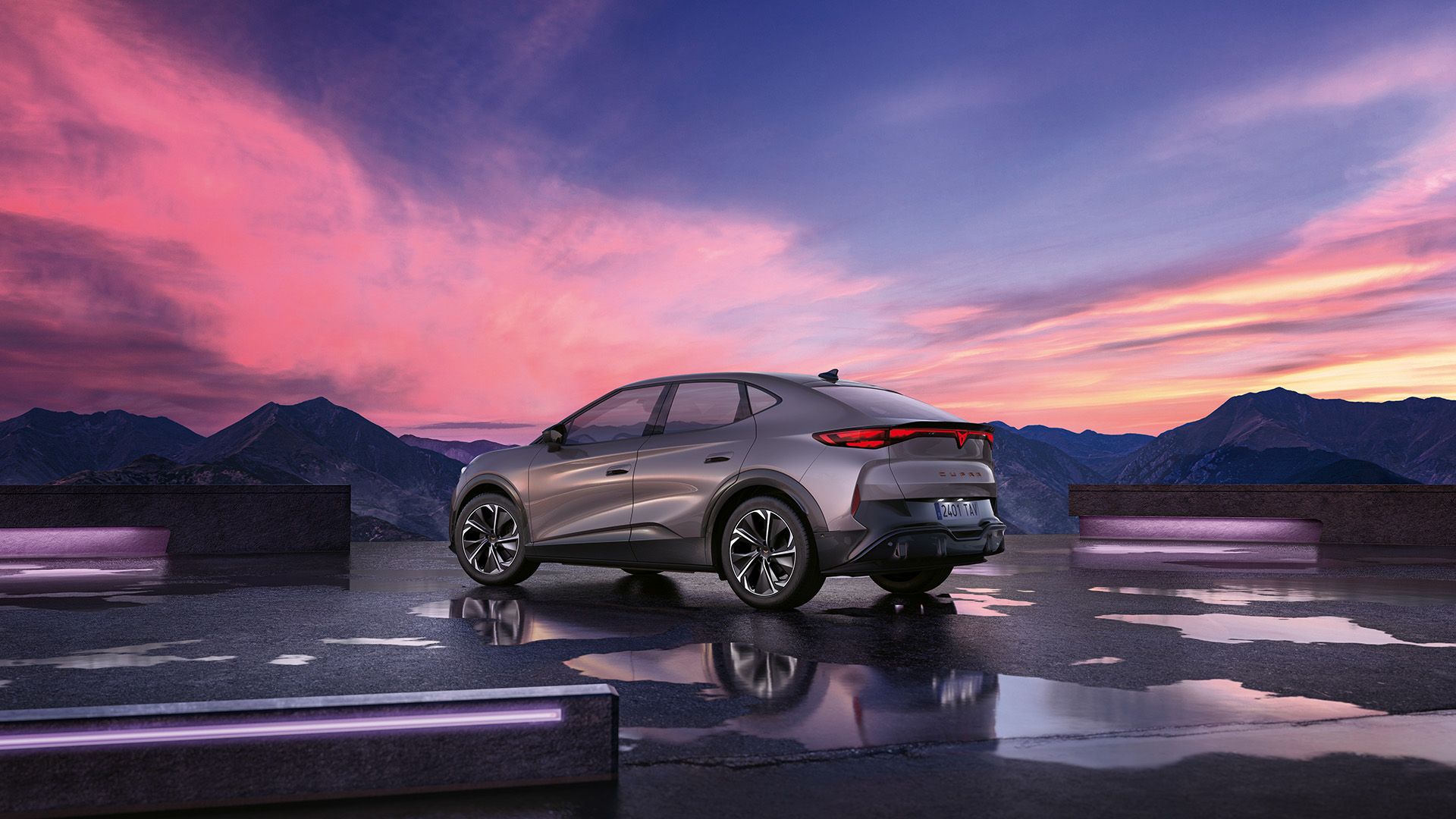 Moderné SUV so šedou metalízou je zaparkované na mokrej ploche s horami v pozadí. Obloha je sfarbená do ružova pri západe slnka. Auto má elegantný dizajn s aerodynamickými líniami.