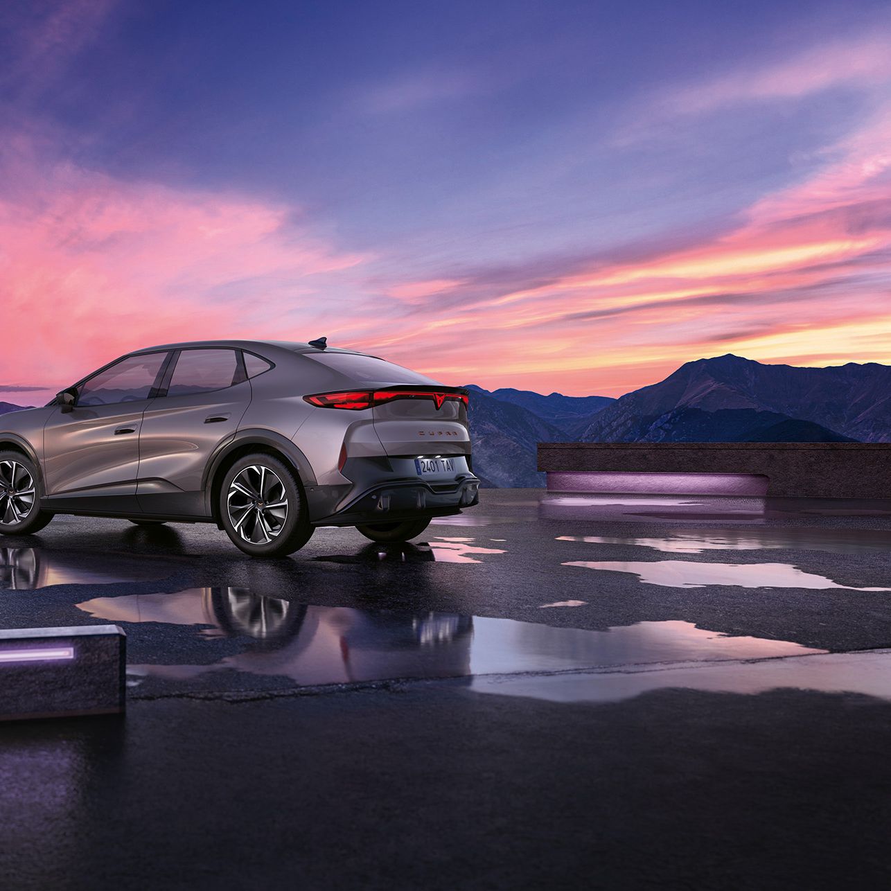 Moderné SUV so šedou metalízou je zaparkované na mokrej ploche s horami v pozadí. Obloha je sfarbená do ružova pri západe slnka. Auto má elegantný dizajn s aerodynamickými líniami.