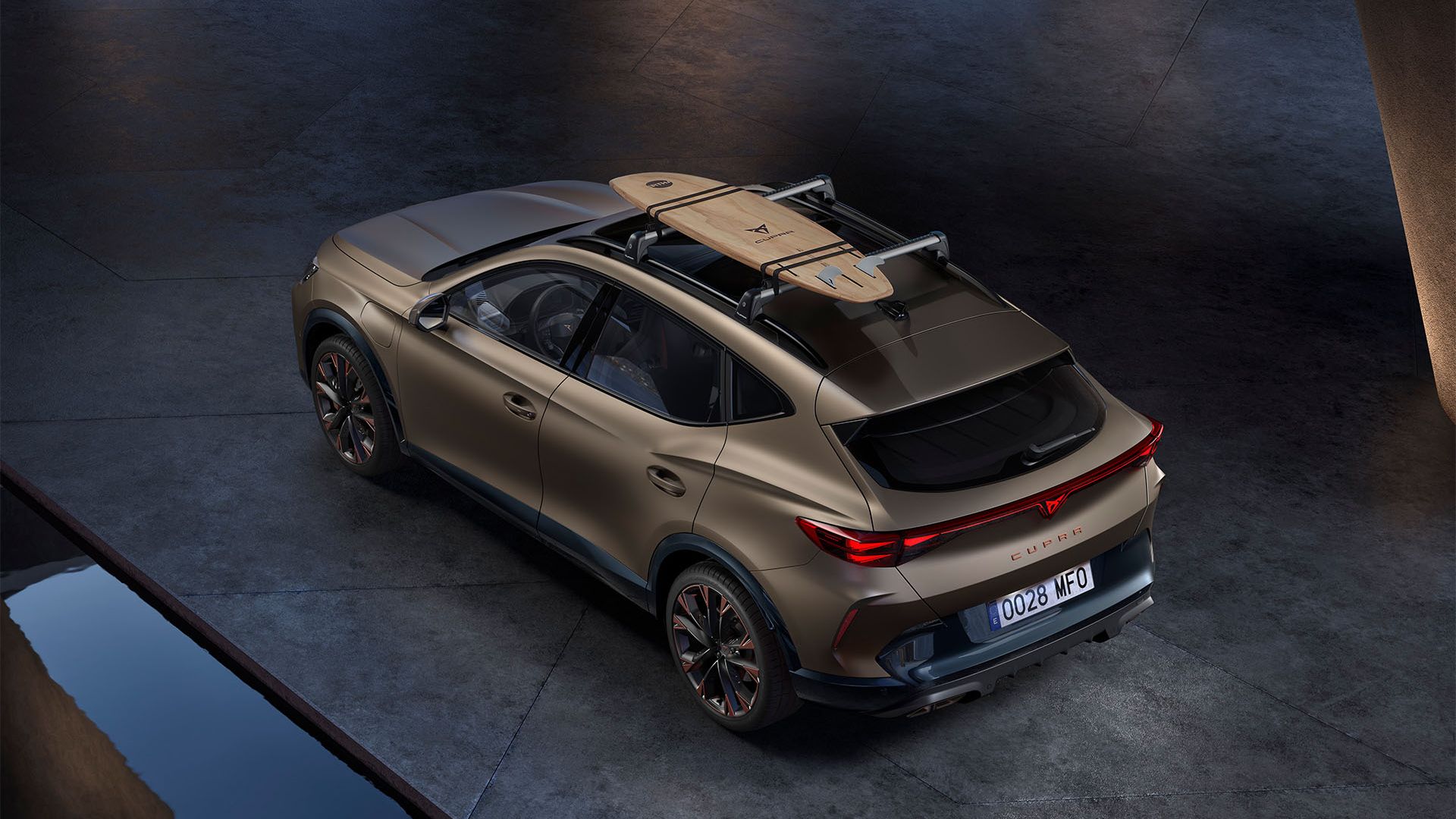 SUV Cupra stojí na betónovej ploche. Na strešnom nosiči je uchytený surf. 