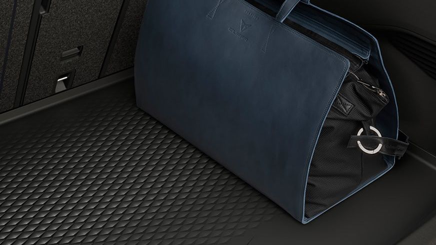 Tmavomodrá cestovná taška umiestnená v batožinovom priestore automobilu. Batožinový priestor má polotuhú vaničku.