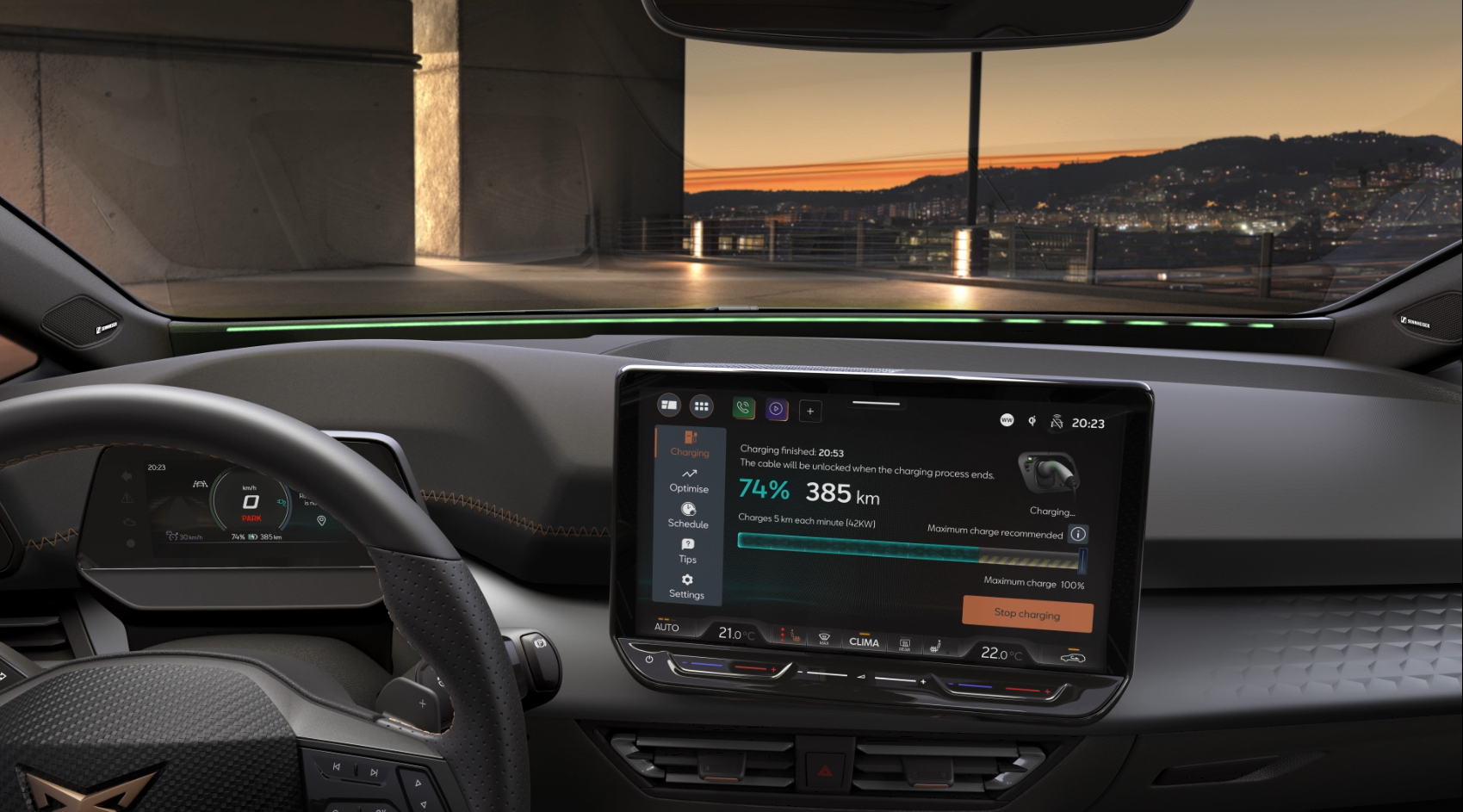 Interiér moderného auta so zapnutým displejom systému infotainment zobrazuje informácie o nabíjaní batérie. Za oknom je panoramatický výhľad na mesto pri západe slnka. Displej ukazuje aktuálny dojazd vozidla na úroveň 385 km pri 74% nabití batérie.