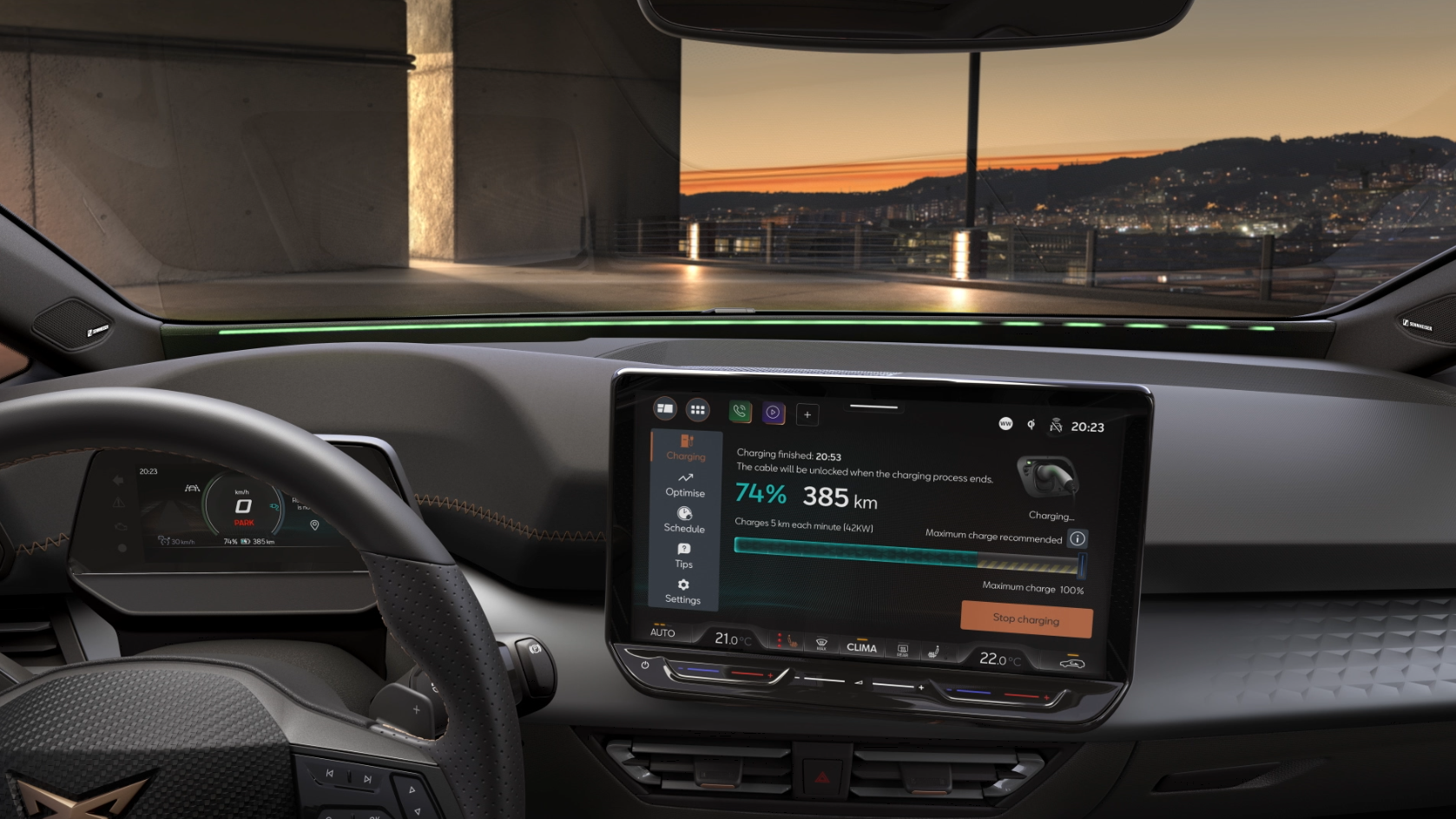 Interiér moderného auta so zapnutým displejom systému infotainment zobrazuje informácie o nabíjaní batérie. Za oknom je panoramatický výhľad na mesto pri západe slnka. Displej ukazuje aktuálny dojazd vozidla na úroveň 385 km pri 74% nabití batérie.
