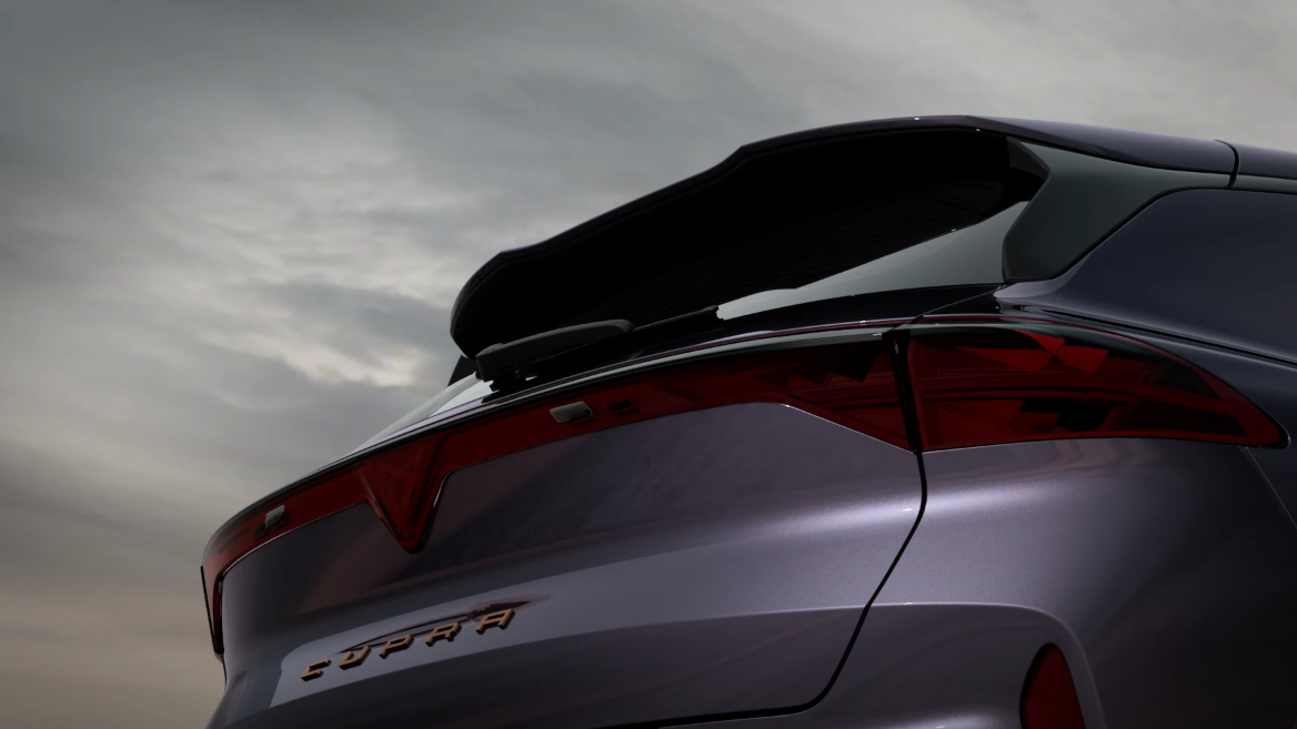 Detail zadnej časti športového automobilu, v popredí je vidieť výrazný spoiler. Na zadných dverách je označenie "CUPRA". Pozadie je pokryté oblakmi a jemným večerným svetlom.