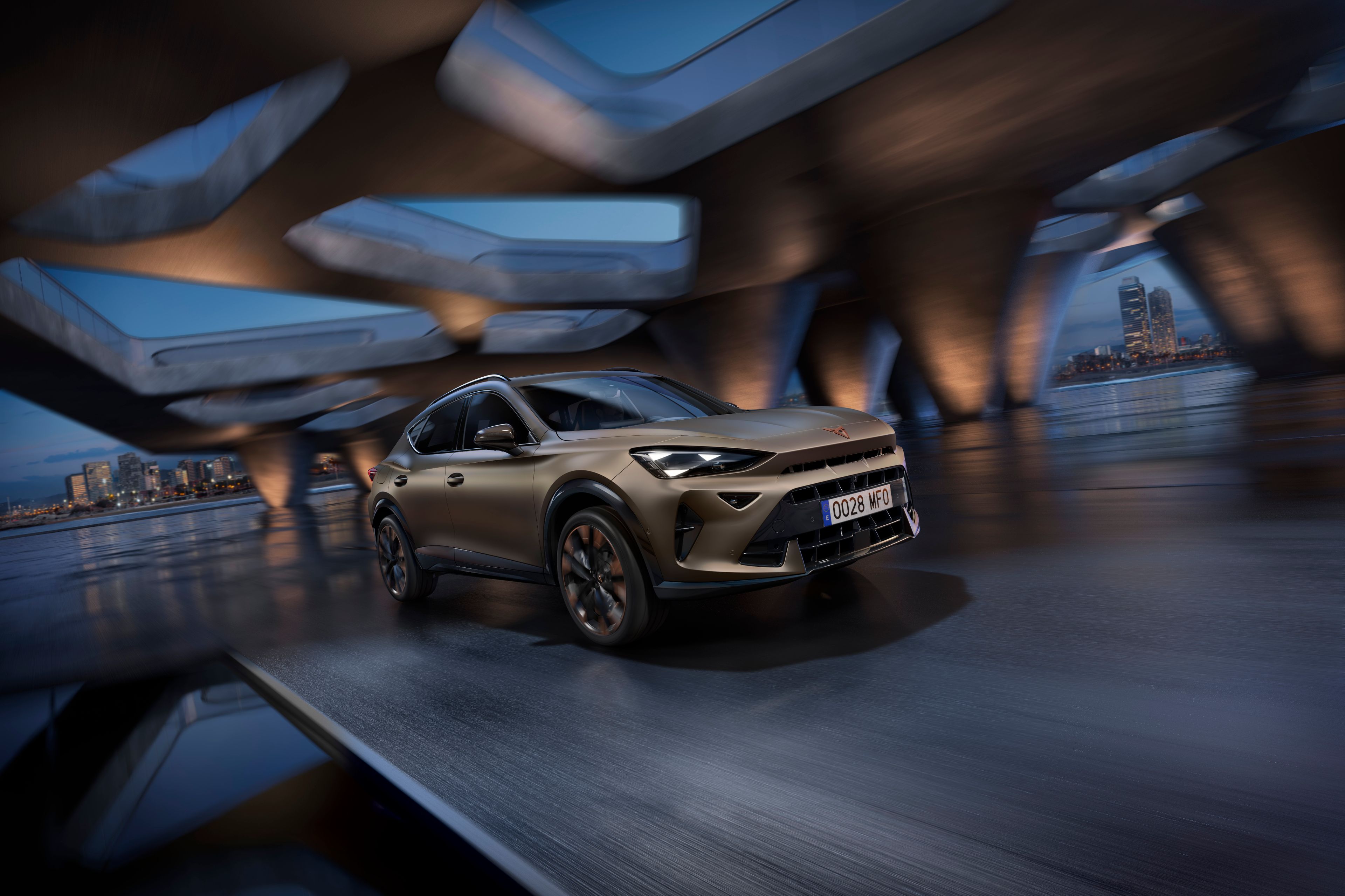 Moderné SUV auto jazdí po moste v noci, mestská panoráma viditeľná v diaľke. Auto je osvetlené reflektormi, ktoré zvýrazňujú jeho štýlový dizajn. Skyline mesta je rozmazaný, čo naznačuje vysokú rýchlosť vozidla.