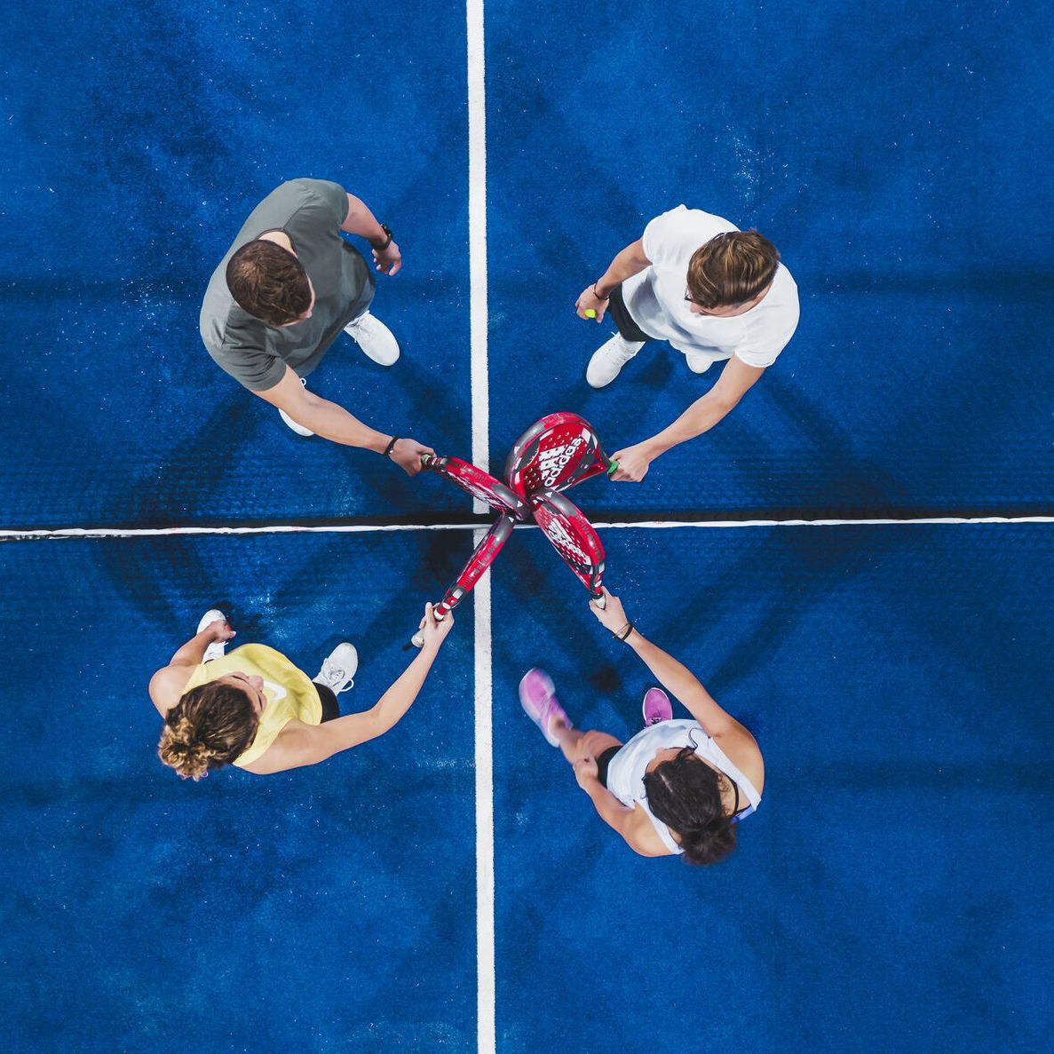 Štyria hráči si podávajú rakety na kurte na začiatku alebo na konci zápasu. Modrý povrch kurtu a biela čiara rozdeľujú ihrisko na polovicu. Hráči sú usporiadaní do párov a stoja oproti sebe.