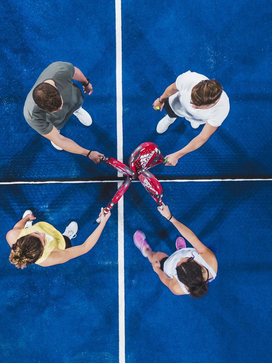 Štyria hráči si podávajú rakety na kurte na začiatku alebo na konci zápasu. Modrý povrch kurtu a biela čiara rozdeľujú ihrisko na polovicu. Hráči sú usporiadaní do párov a stoja oproti sebe.