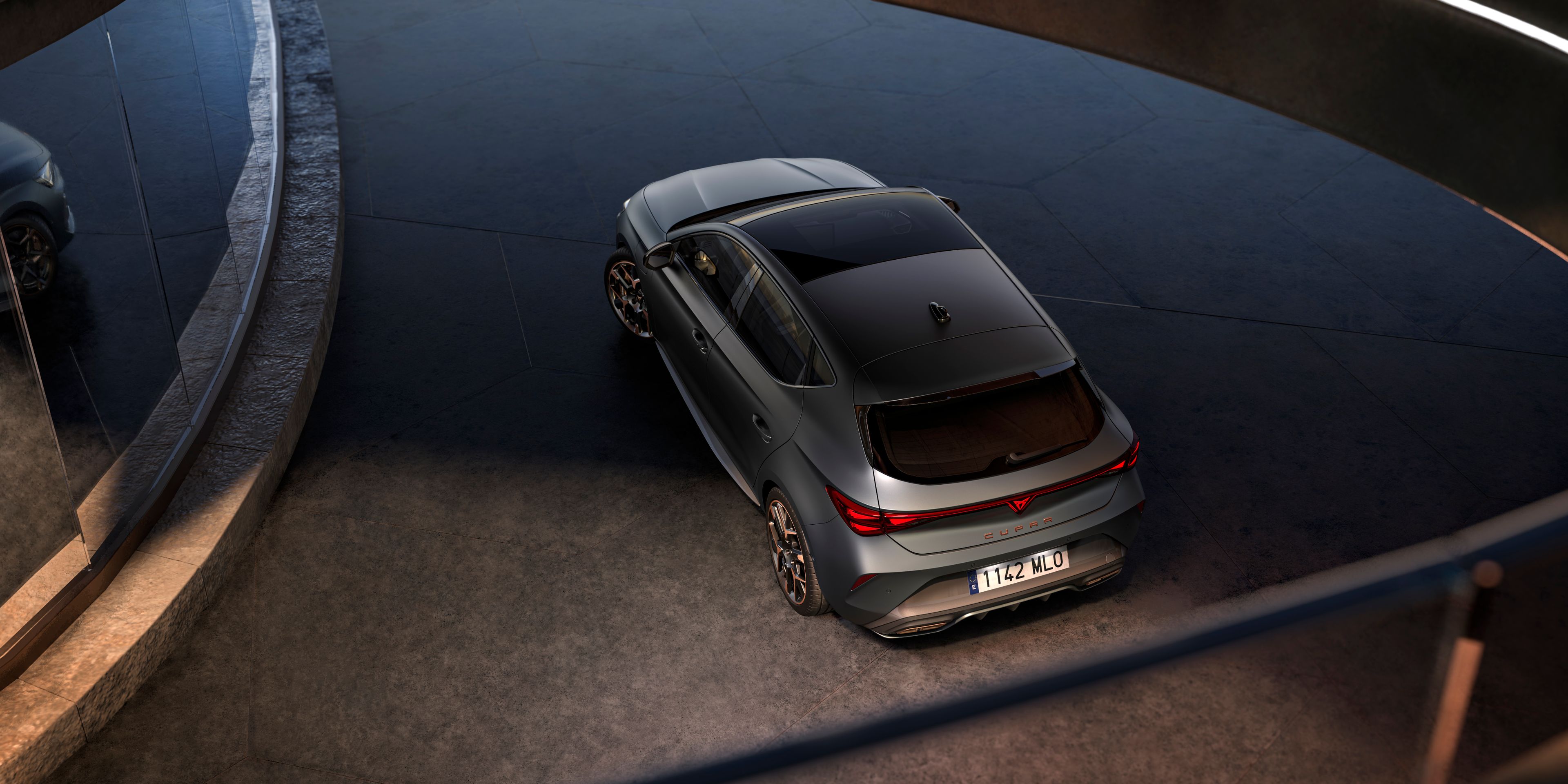 CUPRA Leon zaparkovaný pred sklenenou stenou modernej, futuristickej budovy.