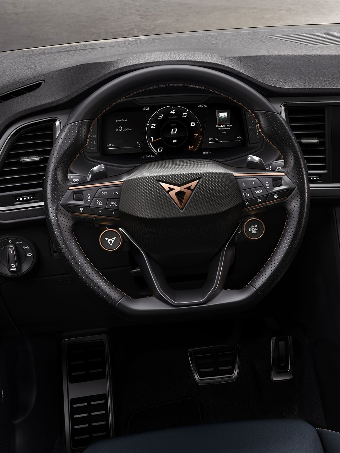 Multifunkčný volant automobilu s množstvom ovládacích prvkov a digitálny prístrojový panel za ním. V strede volantu je logo automobilovej značky. 