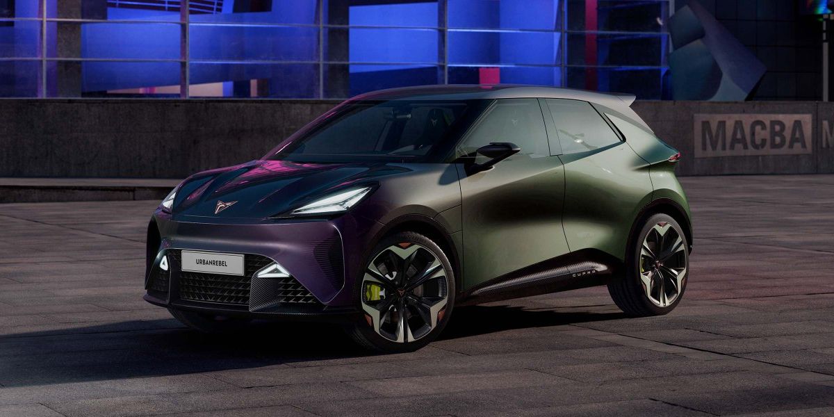Moderné elektrické auto značky CUPRA zaparkovaný v nočnom meste. Auto má tmavú metalickú farbu a športový dizajn. V pozadí je mestská architektúra osvetlená farebnými svetlami.
