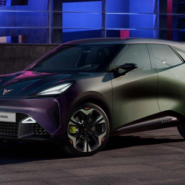 Moderné elektrické auto značky CUPRA zaparkovaný v nočnom meste. Auto má tmavú metalickú farbu a športový dizajn. V pozadí je mestská architektúra osvetlená farebnými svetlami.